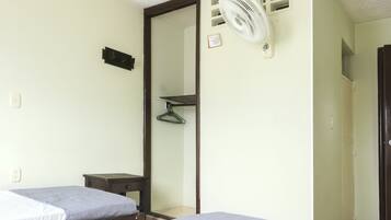 A room with two beds, a small table, a mirror, a fan, and a door leading to another room.