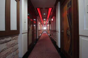 A hotel hallway with a red carpet, wooden doors, and stone walls. - Utopia Motel (Gumi)