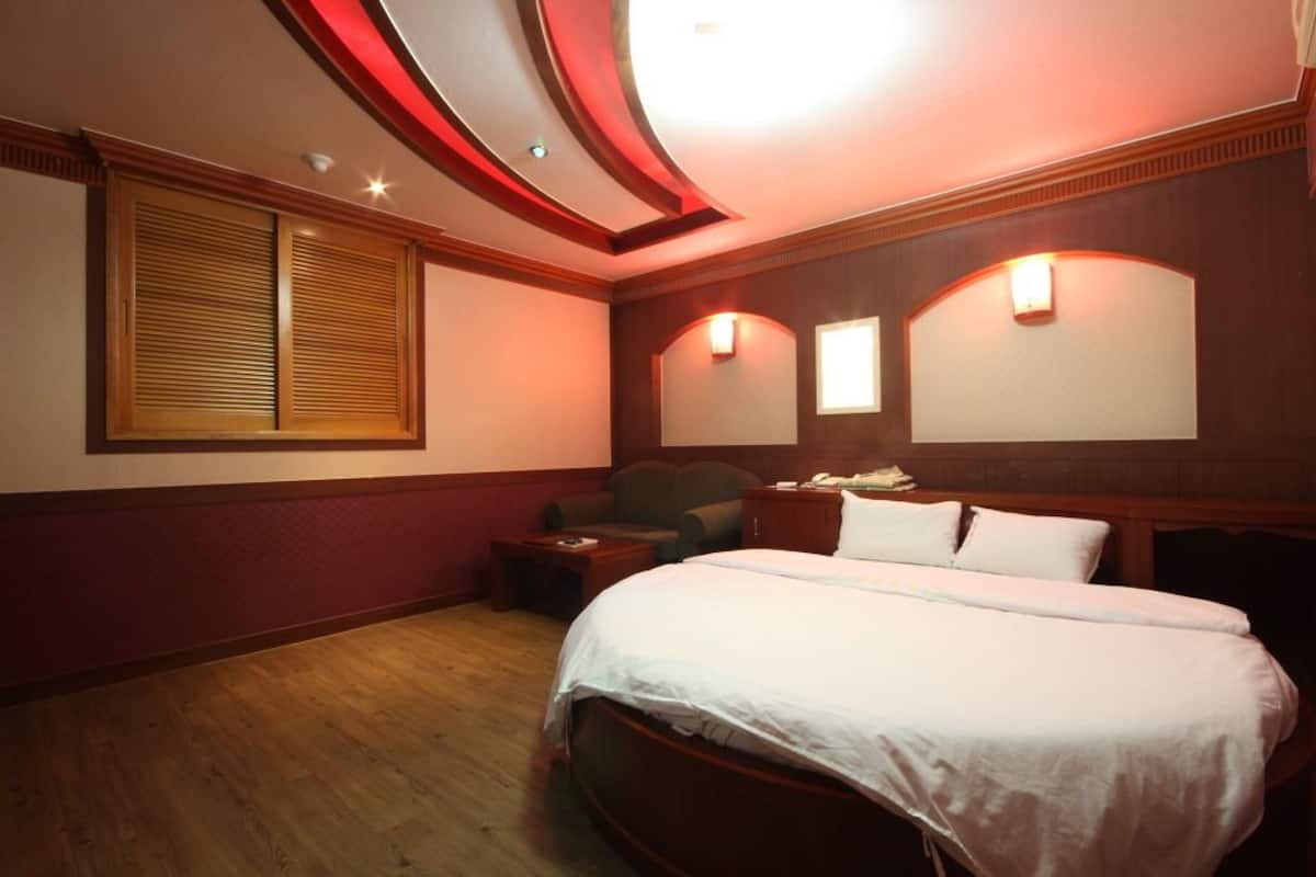 A hotel room with a large bed, a desk, a chair, and a window with blinds.
