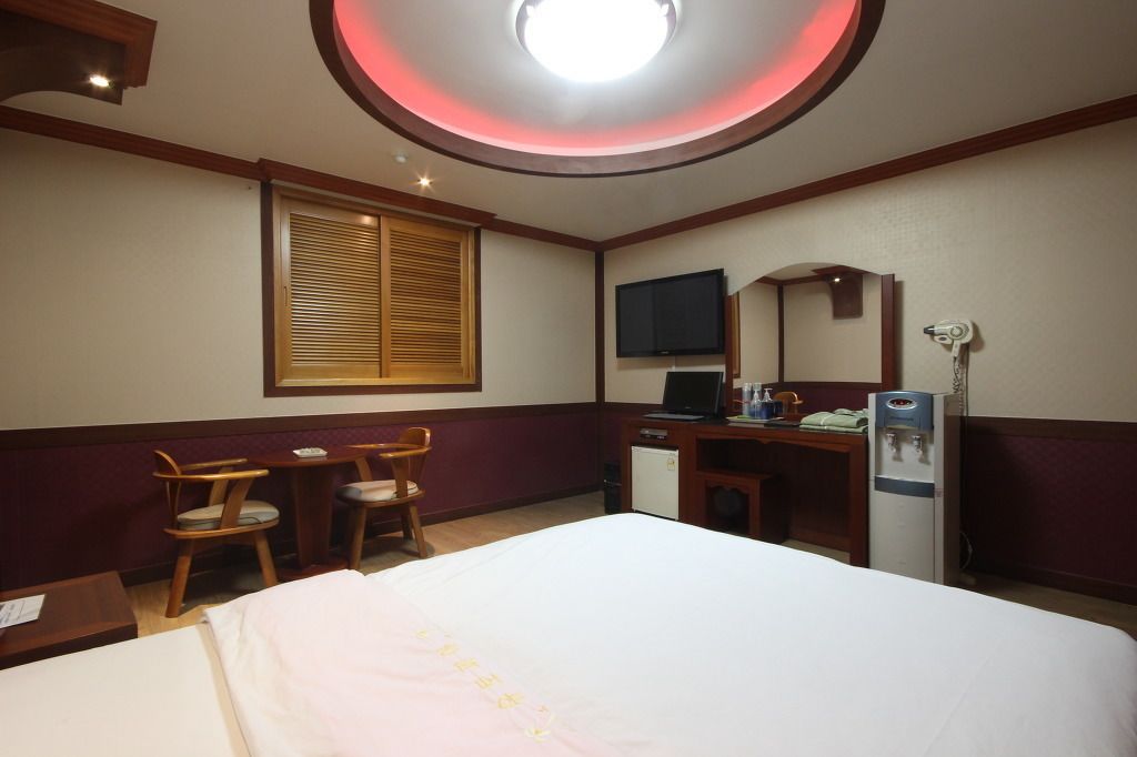 Een hotelkamer met een bed, bureau, stoel, televisie, spiegel en een waterdispenser.