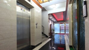 A modern hotel lobby with a marble floor, a reception desk, and a glass elevator.