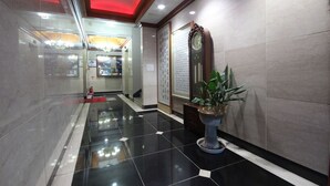 A hotel lobby with a polished black and white tiled floor, a large traditional clock, and a potted plant.