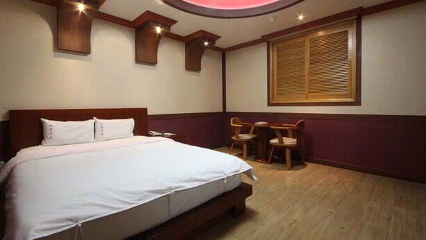 A hotel room with a large bed, a desk, two chairs, a window with blinds, and a ceiling light.