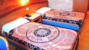 Quarto com duas camas, cada uma com colcha estampada, cabeceira de madeira, parede de pedra e piso de madeira.