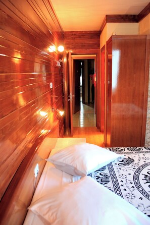 A hotel room with wooden paneling, a bed with patterned bedding, and a door leading to another room. - MindelHotel (Mindelo)