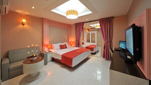 A modern hotel room with a large bed, a sofa, a desk with a TV, and a ceiling light.