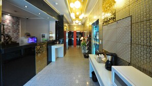 A hotel lobby with a reception desk, a coffee station, and a patterned wall.