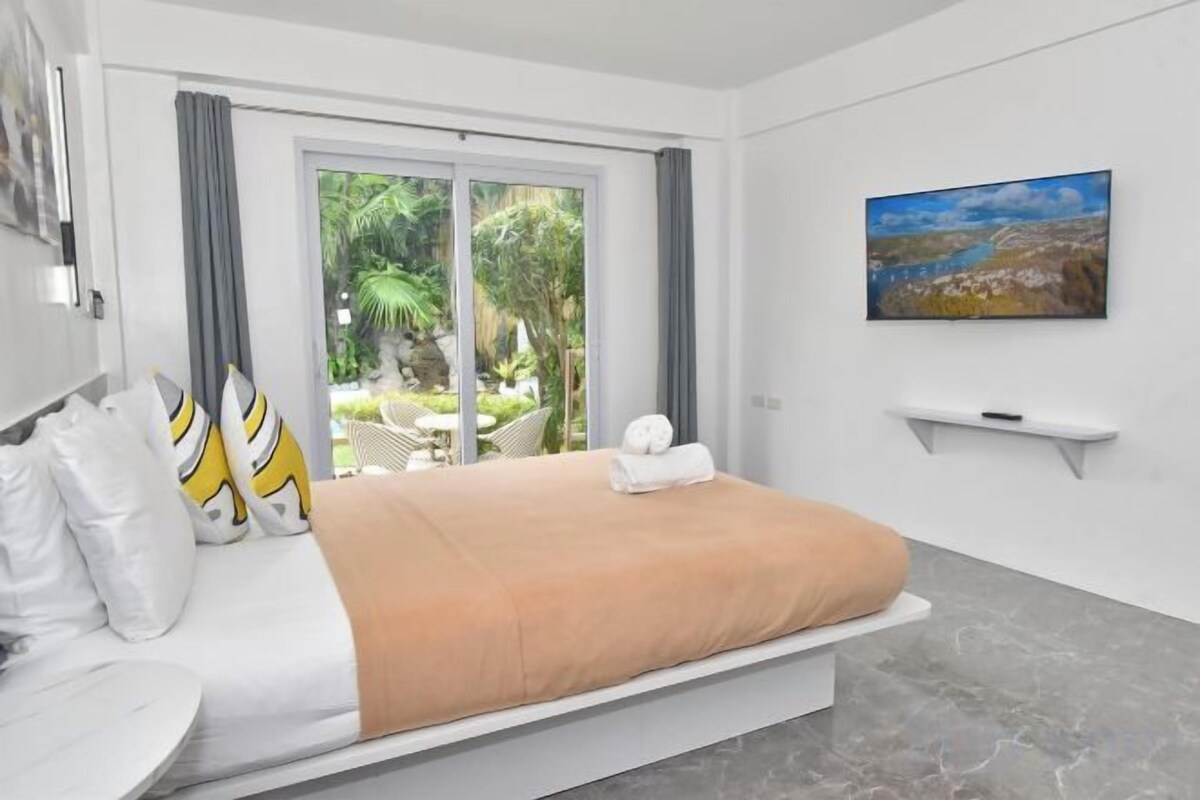 A hotel room with a bed, a TV, a painting, and a view of the outdoors.