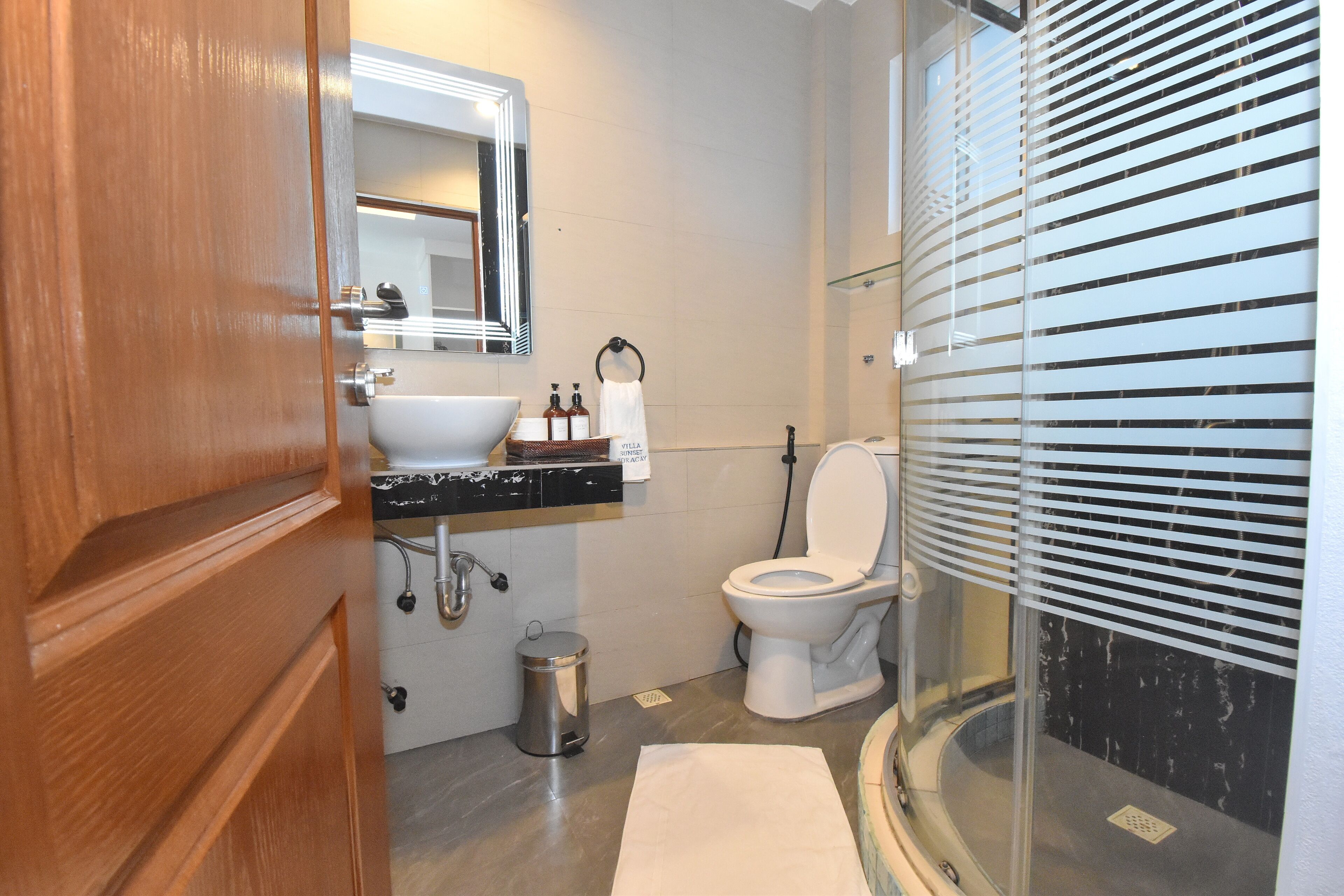 Ein Badezimmer mit Holztür, Waschbecken, Toilette und Duschbereich mit Milchglasüren.