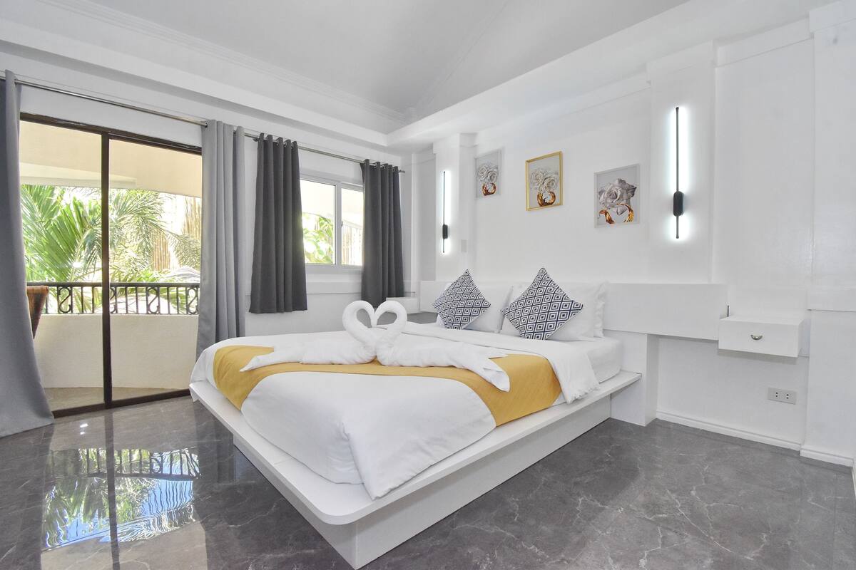 Una habitación de hotel moderna con una cama grande, un balcón con cortinas y vistas a zonas verdes.