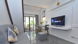 Un salón moderno con un sofá gris, un reposapiés y un televisor de pantalla plana montado en una pared blanca.
