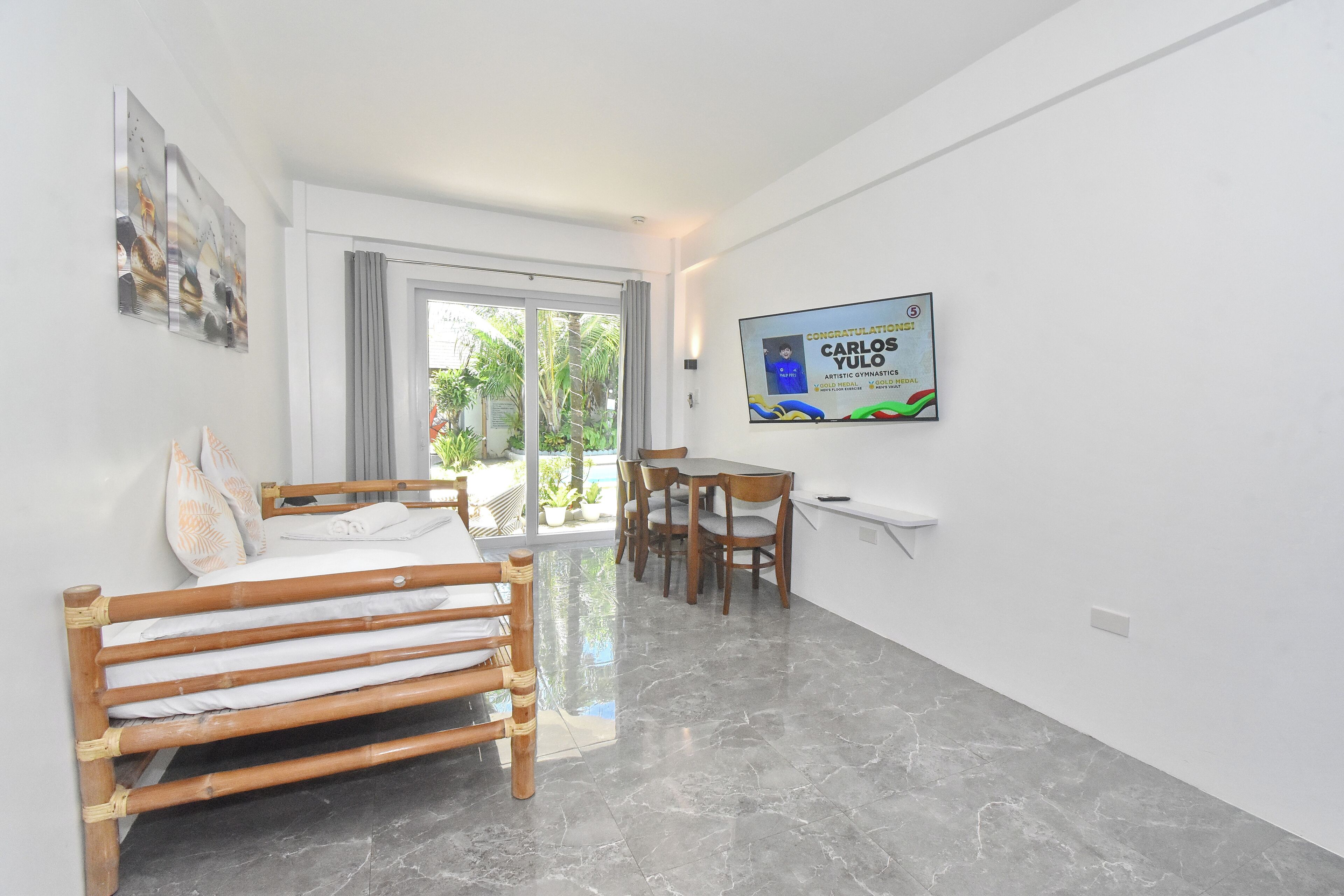 A modern hotel room with a bed, a dining area, and a TV displaying a congratulatory message.