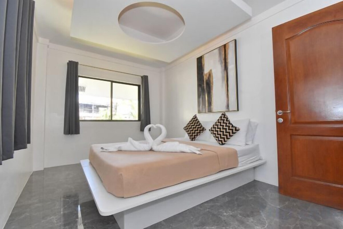 A hotel room with a bed, a window, a door, and a painting on the wall.