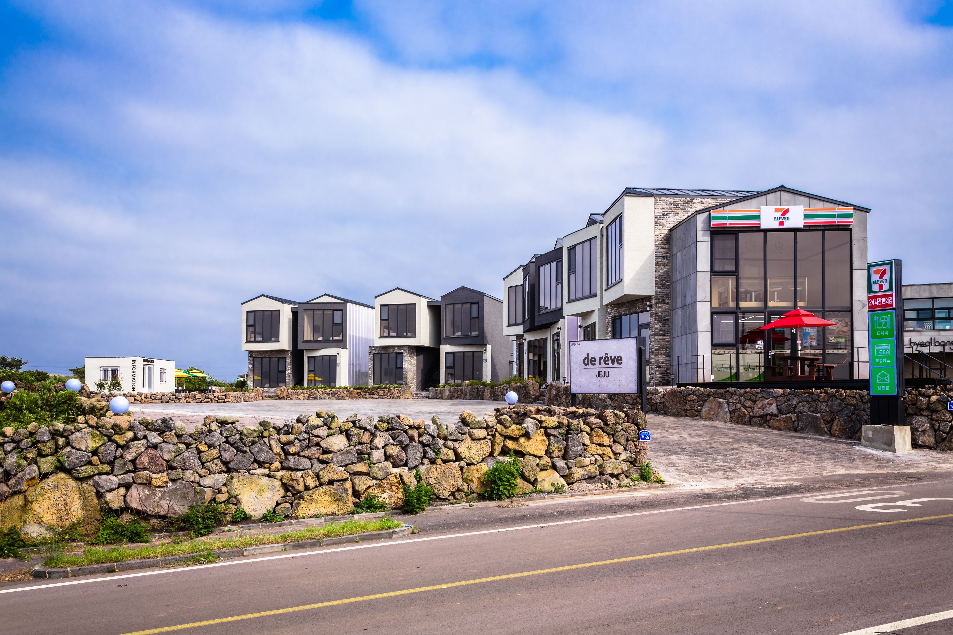 A modern hotel with a 7-Eleven convenience store, stone wall, and outdoor seating area.