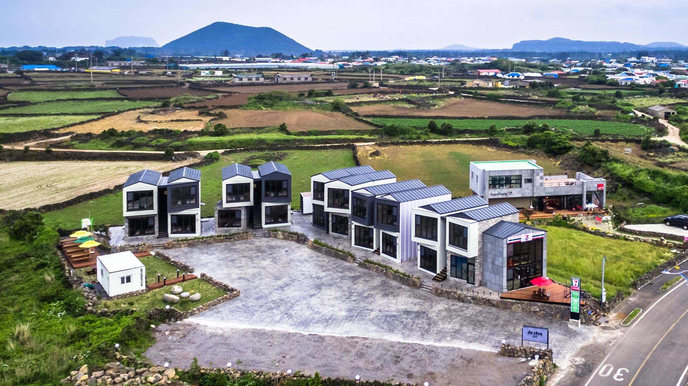 A modern hotel with a central courtyard, surrounded by fields and a mountain in the background.