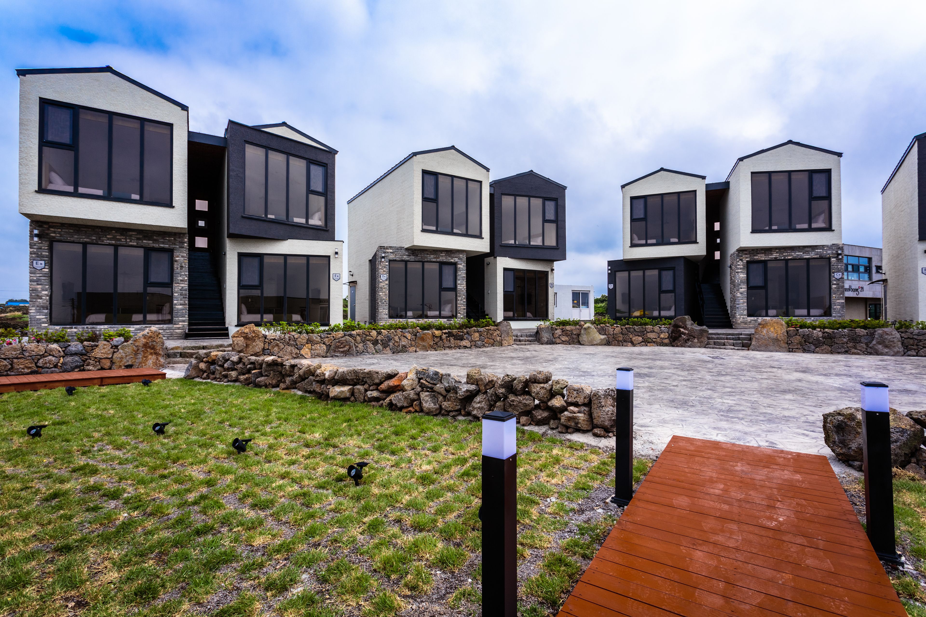 A modern residential complex with multiple two-story houses, a stone retaining wall, and a wooden deck.