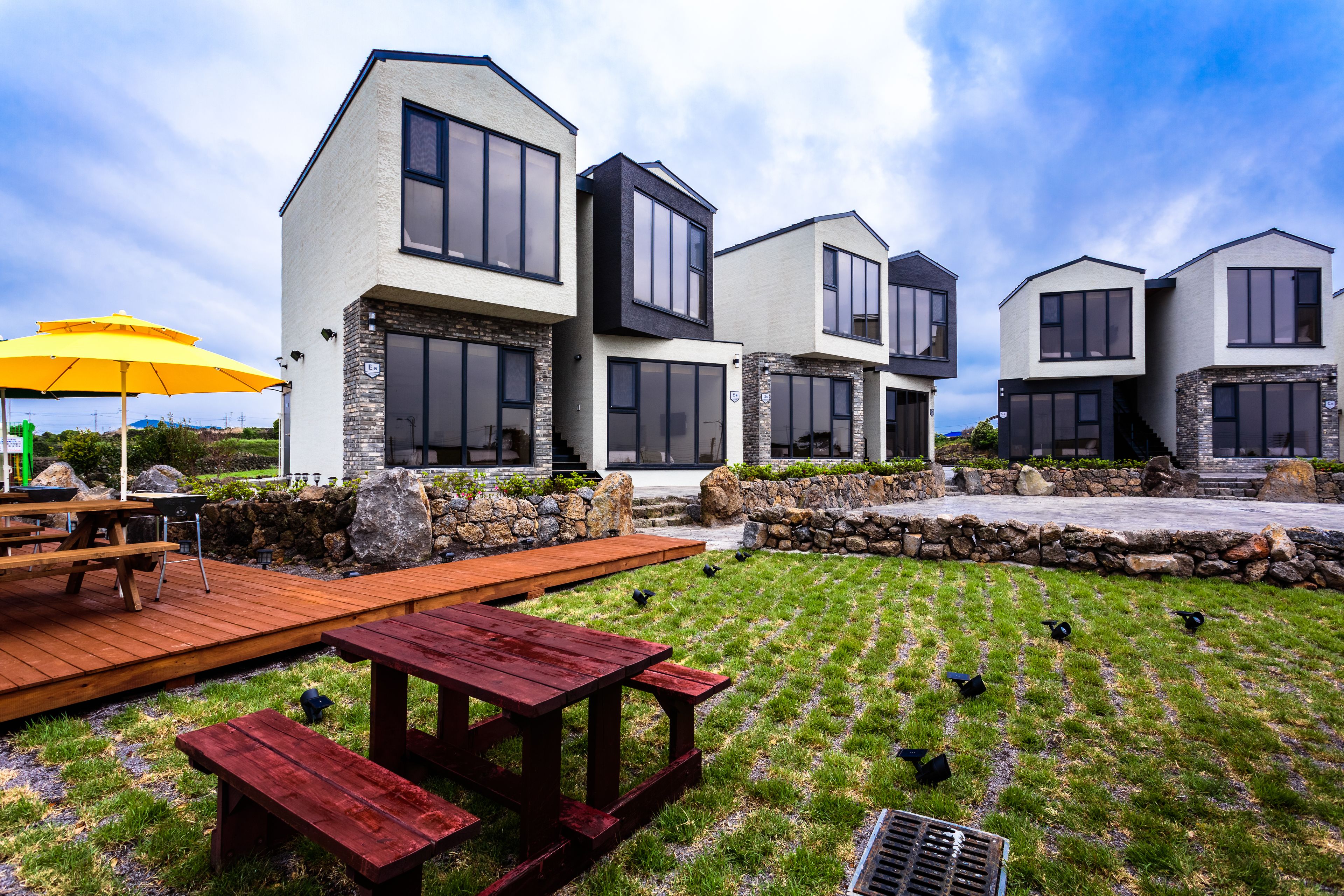 A modern residential complex with multiple houses, a wooden deck, picnic tables, and a grassy lawn.