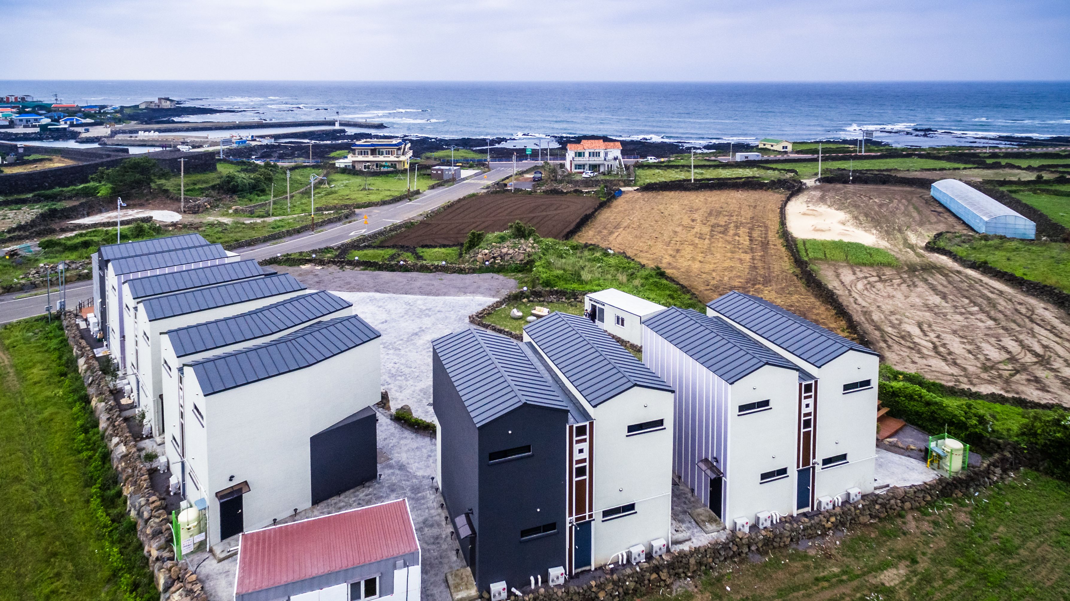 A modern building complex with multiple units, a paved road, and a view of the sea.