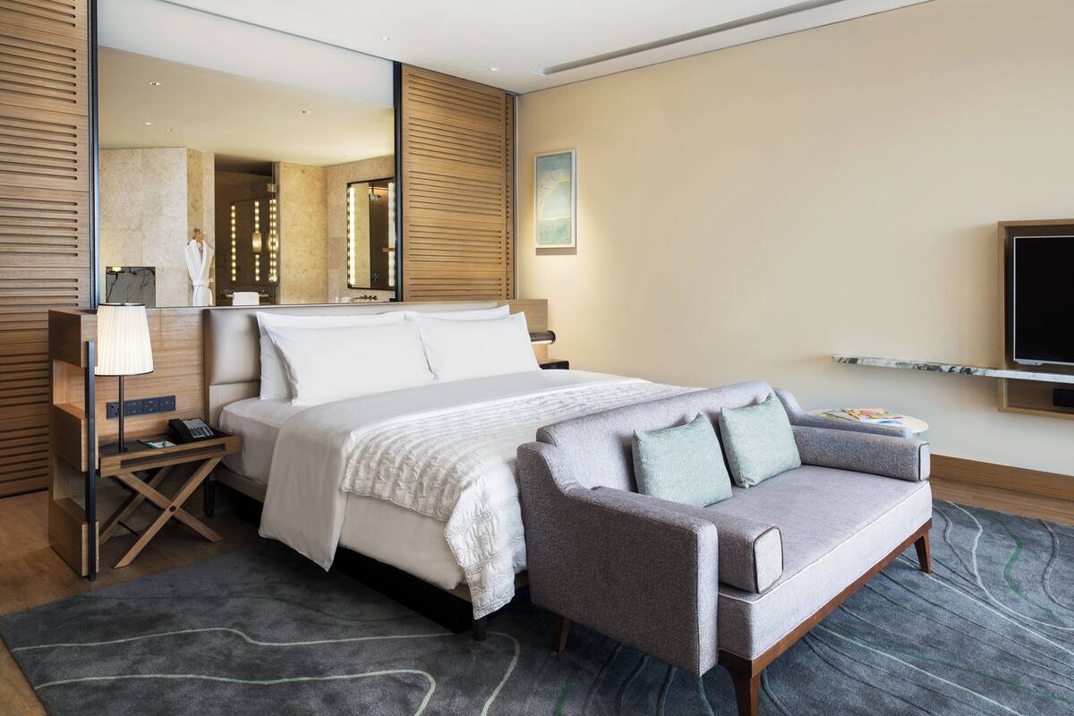 Ein modernes Hotelzimmer mit einem großen Bett, einem grauen Sofa, einem Fernseher und einem Spiegel.
