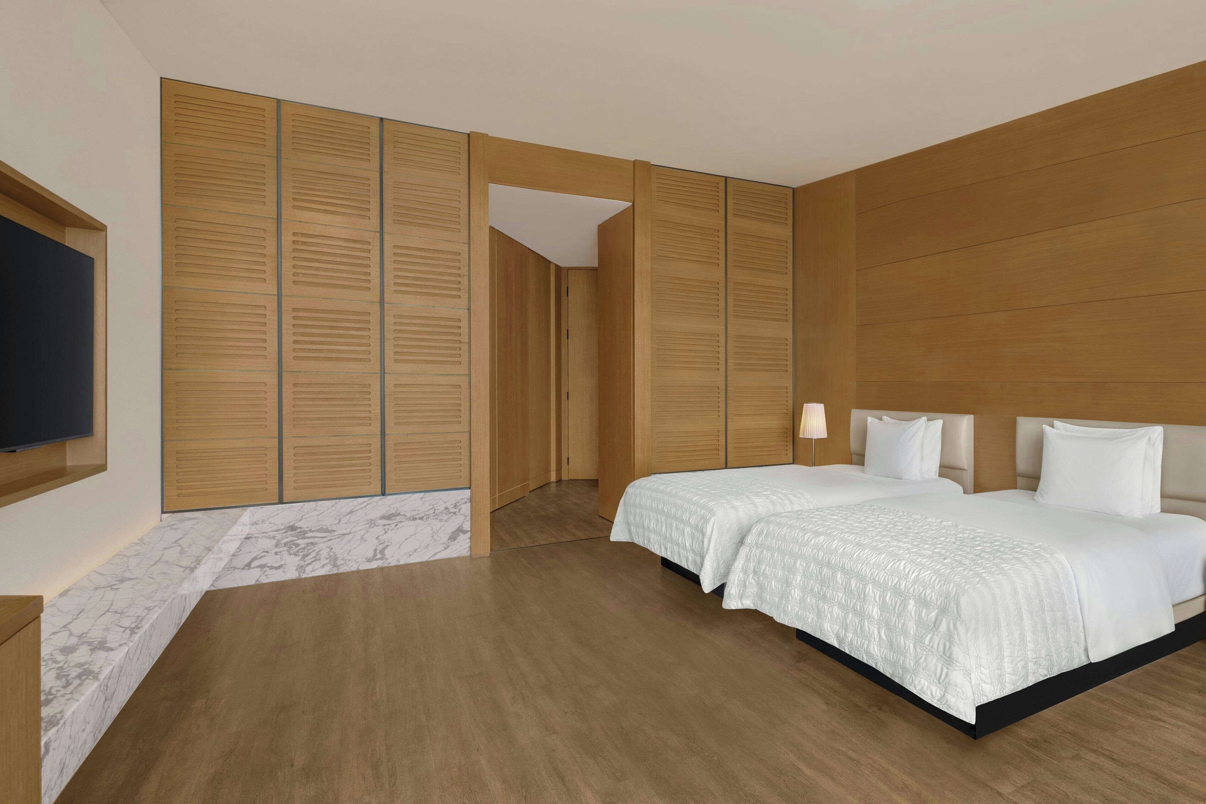 A modern hotel room with a large bed, wooden paneling, a marble accent wall, and a flat-screen TV mounted on the wall.