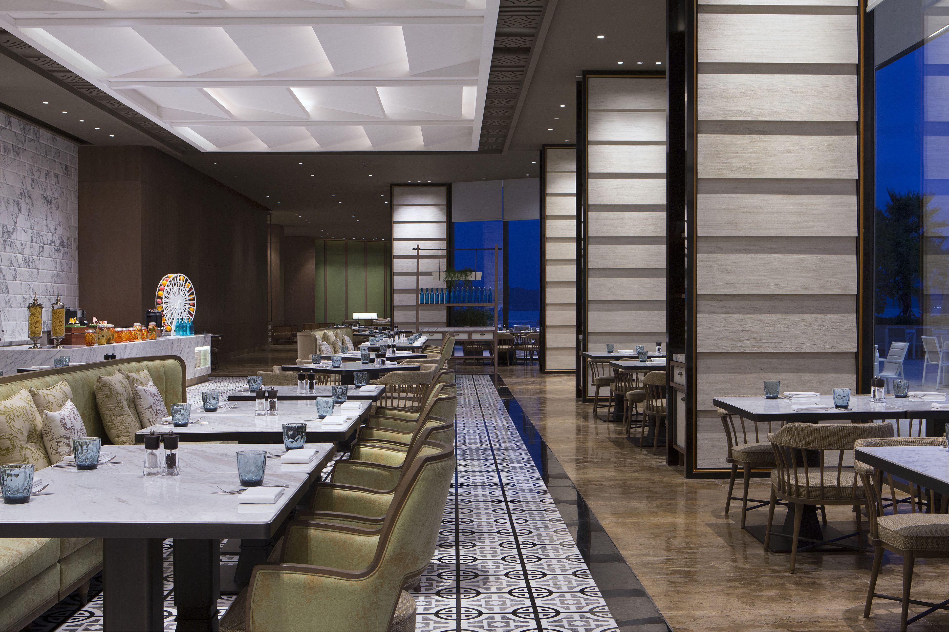 A modern restaurant with a long counter, booths, and tables. There are decorative items on the counter and a patterned floor.