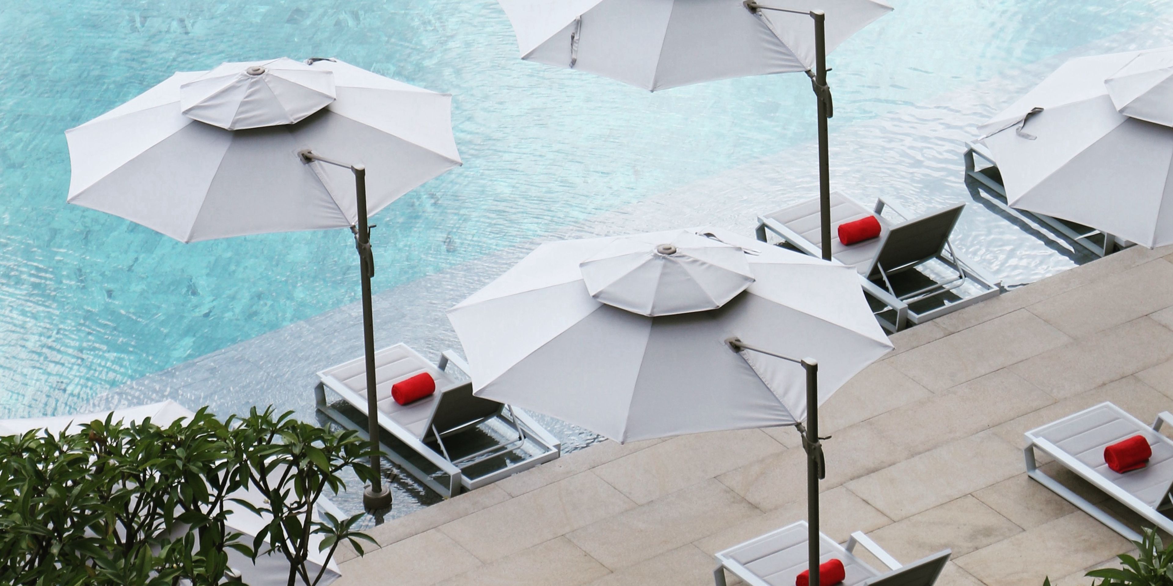 Een zwembadgedeelte met meerdere witte parasols en ligstoelen, waarvan sommigen rode kussens hebben.