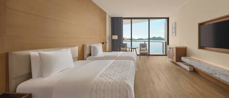A hotel room with two beds, a TV, a desk, and a view of the water.