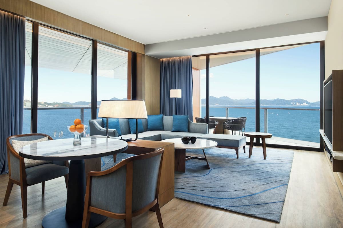 Ein modernes Hotelzimmer mit großem Balkon, einer Couch, einem Esstisch und einem Fernseher.
