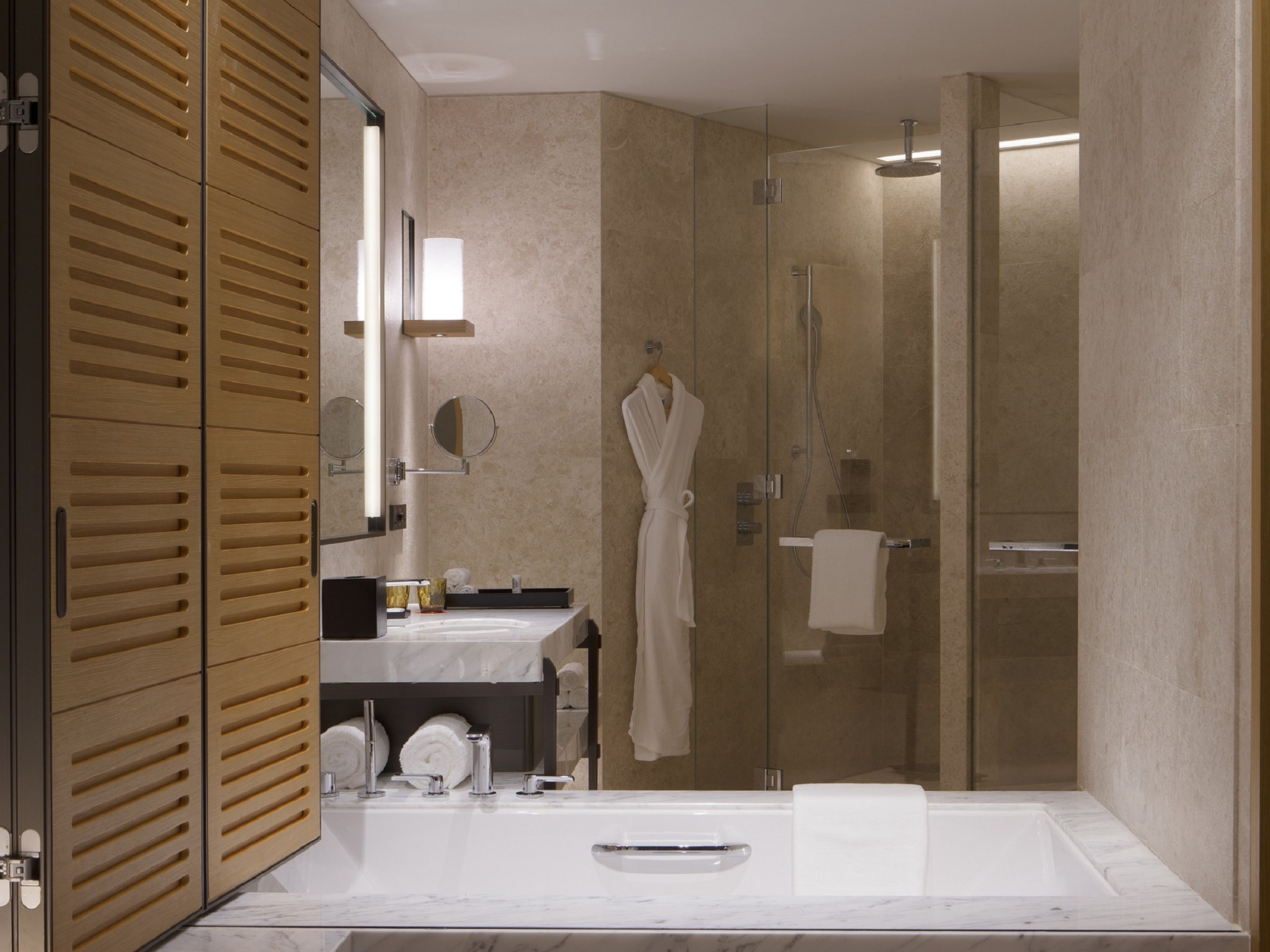 Un baño moderno con un espejo grande, armarios de madera, lavamanos de mármol y una ducha con cerramiento de vidrio.
