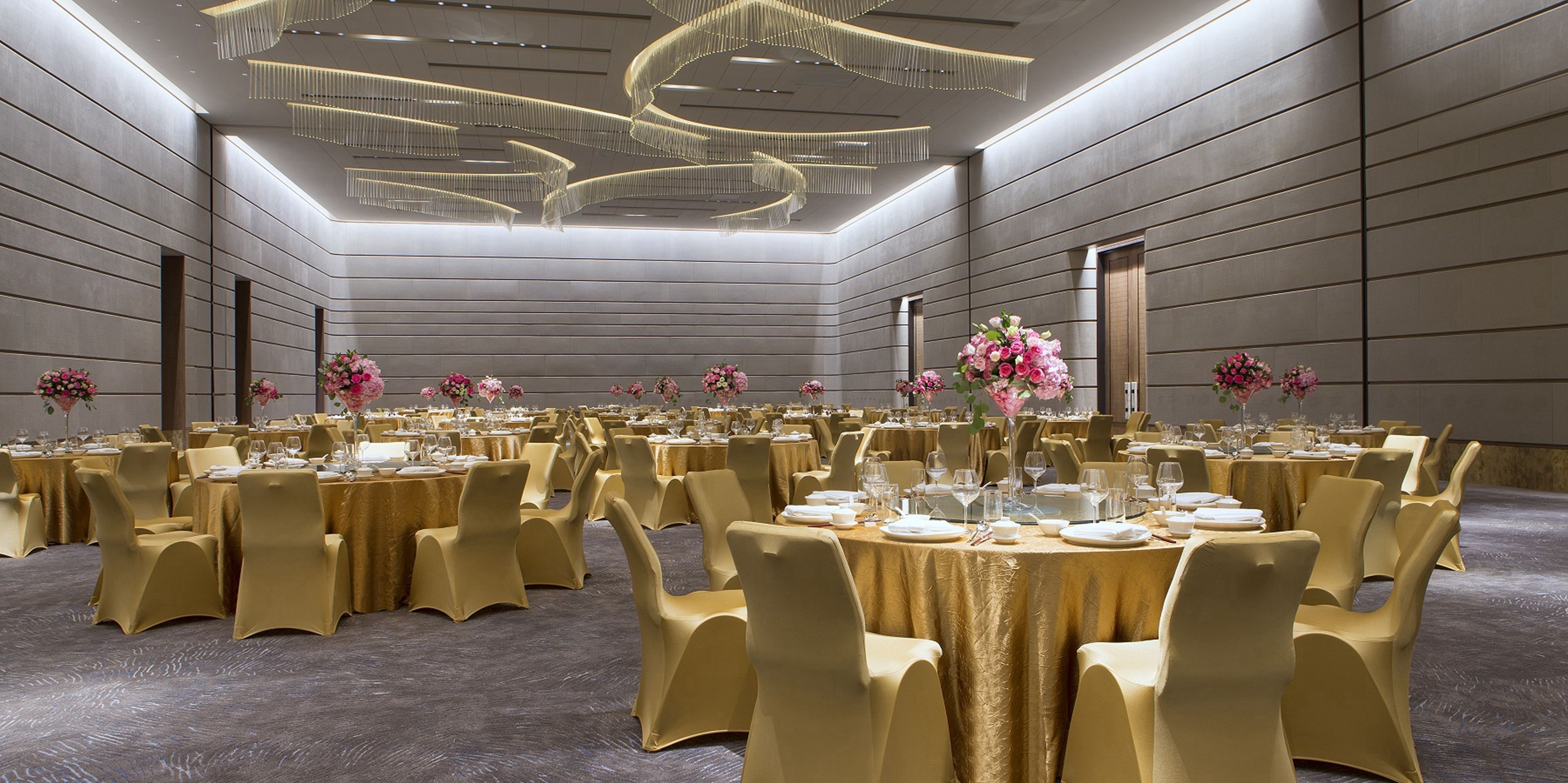 A banquet hall with round tables, gold chairs, and floral centerpieces.