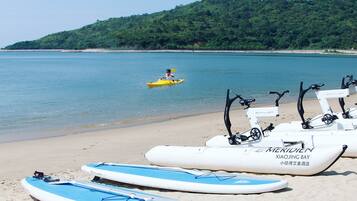 Una playa con kayaks y tablas de remo de pie, una persona kayakendo, y un letrero que dice 'XIAOJING BAY'.