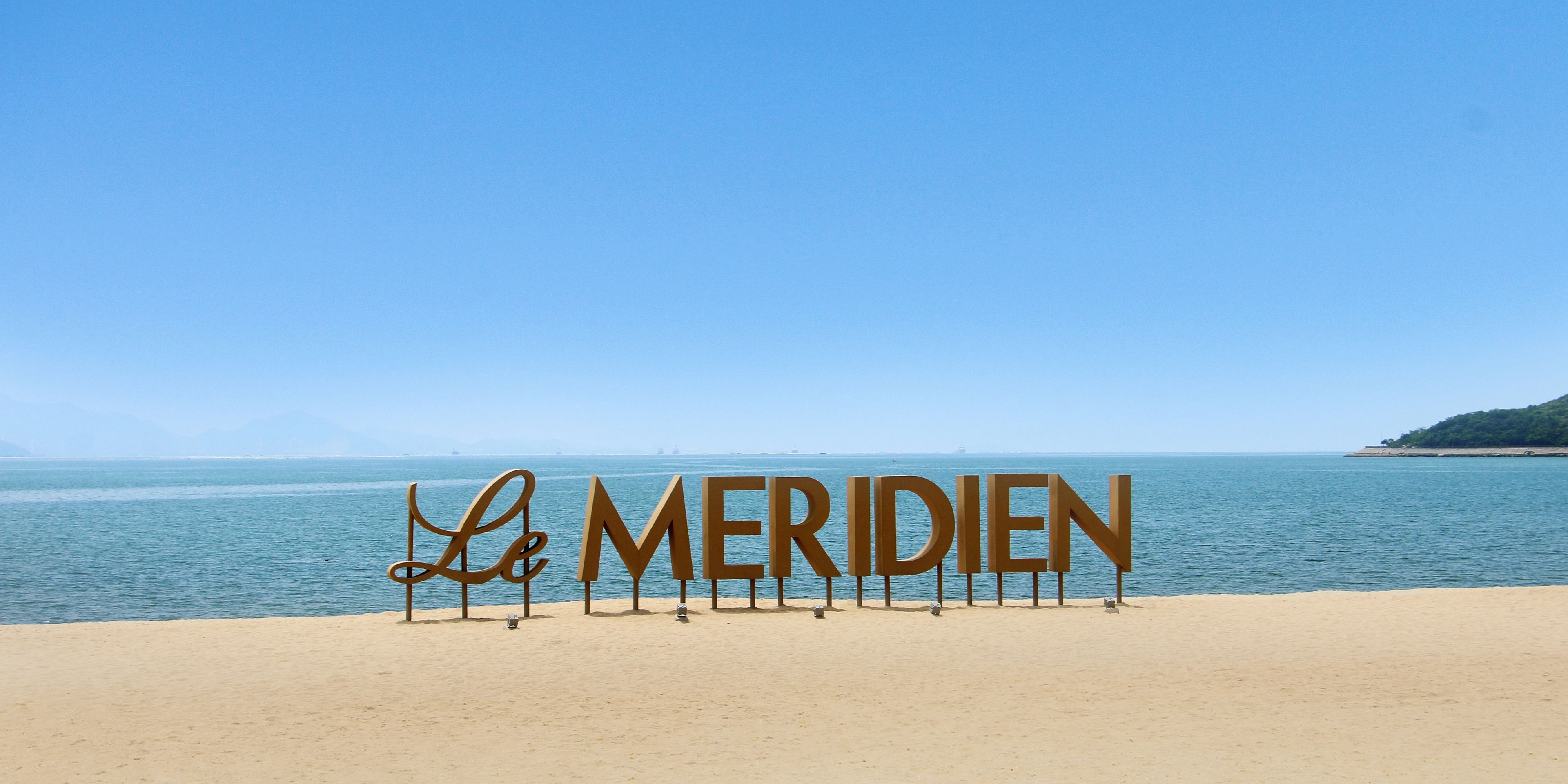 A beach with a large sign reading "Le Meridien" and a clear view of the sea.