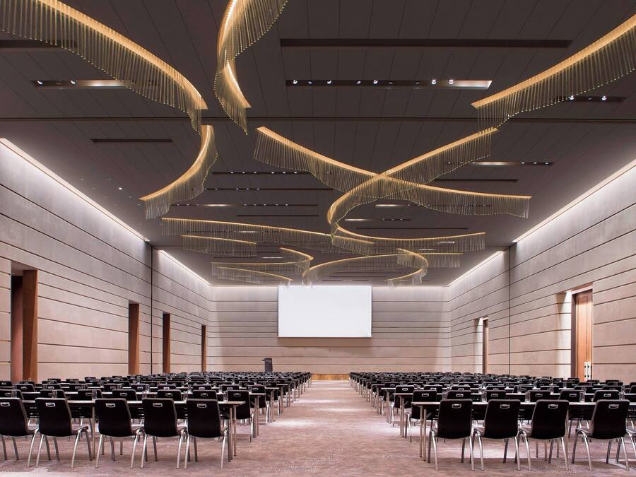 A conference room with rows of chairs, a large screen at the front, and modern ceiling design.