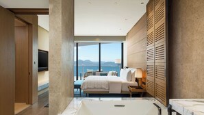 Habitación de hotel moderna con una cama grande, un baño con bañera de mármol y vistas a las montañas.