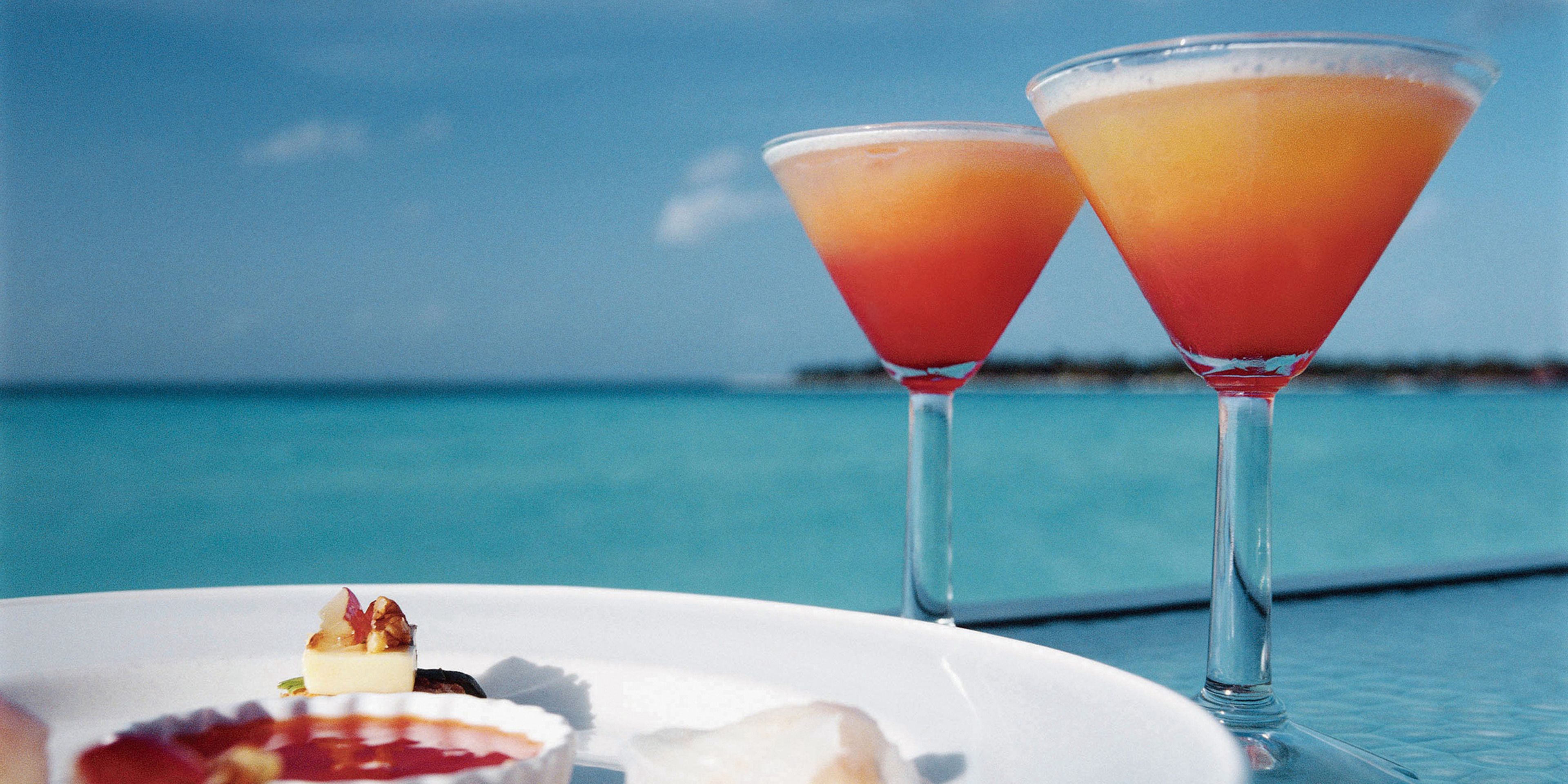Two martini glasses with a tropical drink on a table by the sea.
