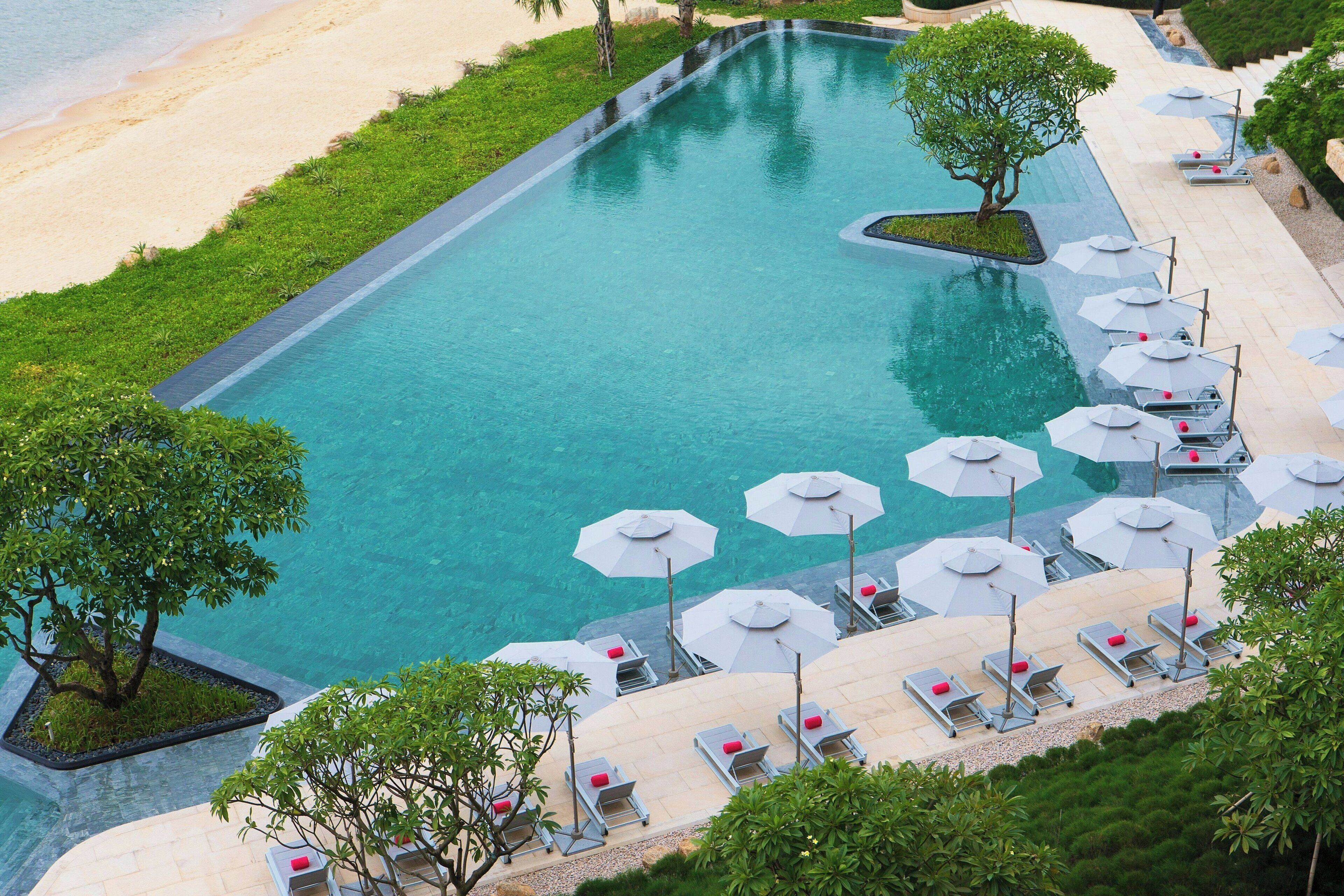 Ein großer Pool mit einer umlaufenden Sonnenterrasse, Liegestühlen und Sonnenschirmen.