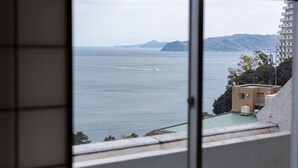 A view through a window of a building overlooking a body of water, with a distant coastline and a mountain range. - Breezbay Seaside Resort Atami (Atami)