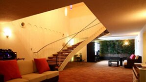 A spacious living area with a wooden floor, a sofa with red cushions, a staircase, and a wall with a green plant. - Breezbay Seaside Resort Atami (Atami)