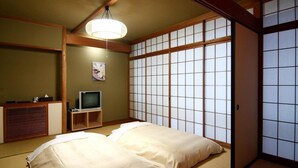 A traditional Japanese room with tatami flooring, a low wooden bed, a television on a wooden stand, and a shoji screen. - Breezbay Seaside Resort Atami (Atami)