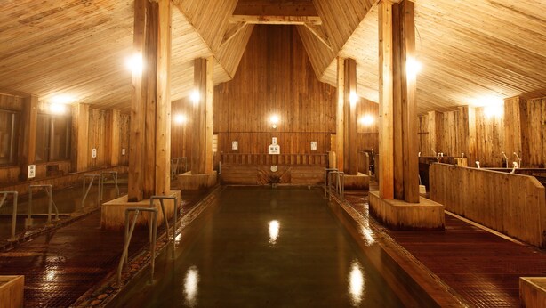 A wooden interior with a central pool, wooden benches, and railings. - Shintamagawa Onsen (Senboku)
