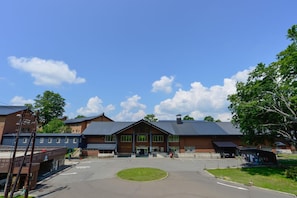 A large building with a central entrance, a parking lot, and a grassy area in front.
