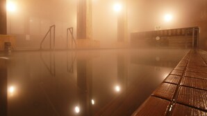 A sauna with a wooden bench and a reflective floor, surrounded by wooden walls and pillars, with bright lights illuminating the space. - Shintamagawa Onsen (Senboku)
