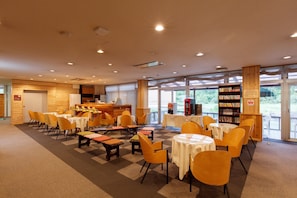 A spacious indoor area with multiple tables and chairs, a coffee station, and a bookshelf.