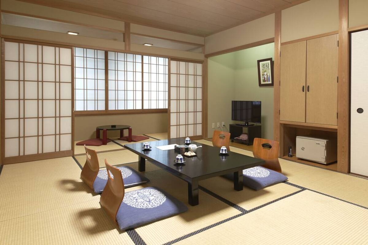 Une pièce avec un sol recouvert de tatamis, une petite table basse, des coussins, un meuble et un téléviseur.