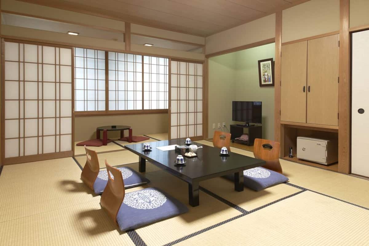 A tatami mat room with a low table, cushions, a cabinet, and a television.