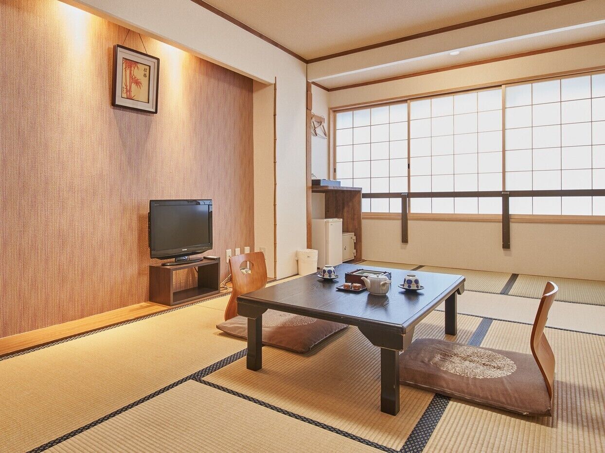 Ein traditioneller japanischer Raum mit Tatami-Bodenbelag, einem niedrigen Tisch, einem Fernseher und einer Schiebetür.