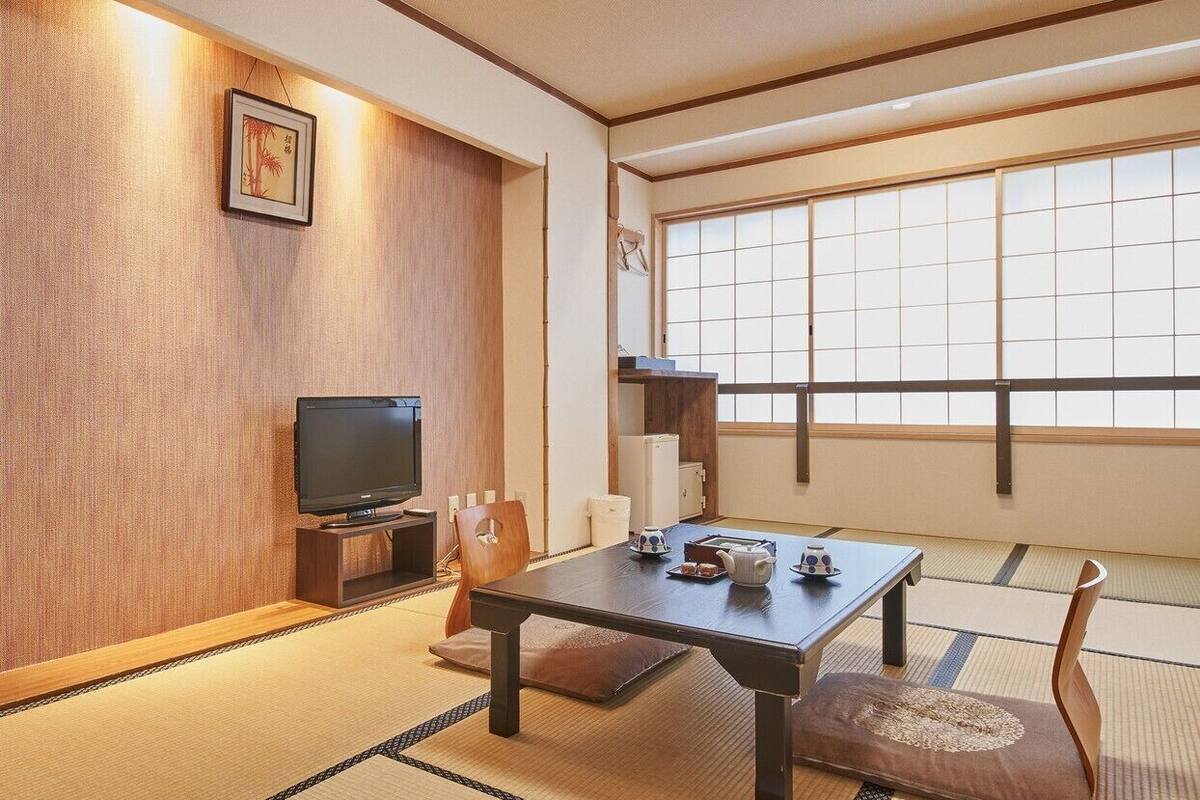 Une pièce de style japonais traditionnel, avec un sol recouvert de tatamis, une table basse, un téléviseur et une porte coulissante.