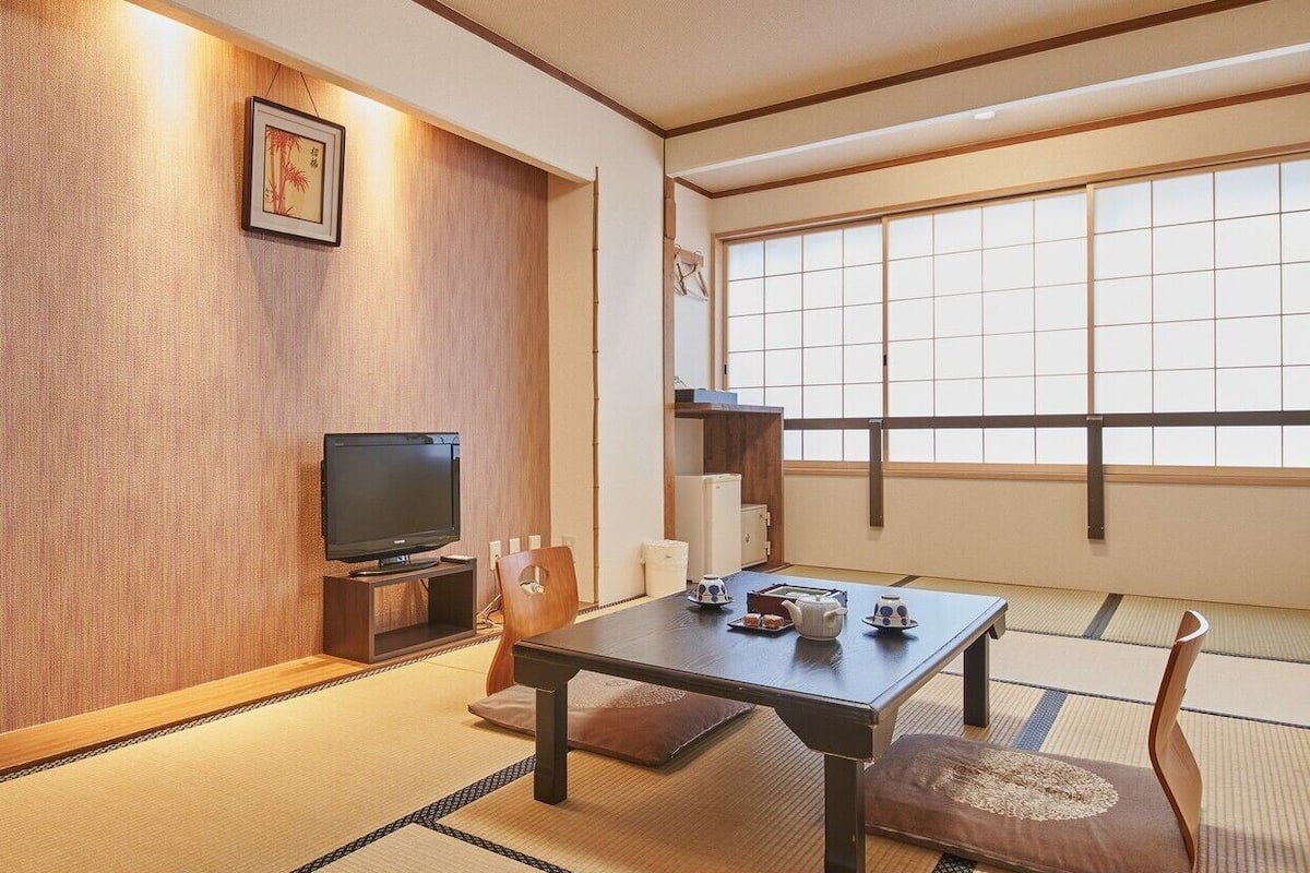 A traditional Japanese room with tatami flooring, a low table, a television, and a sliding door.