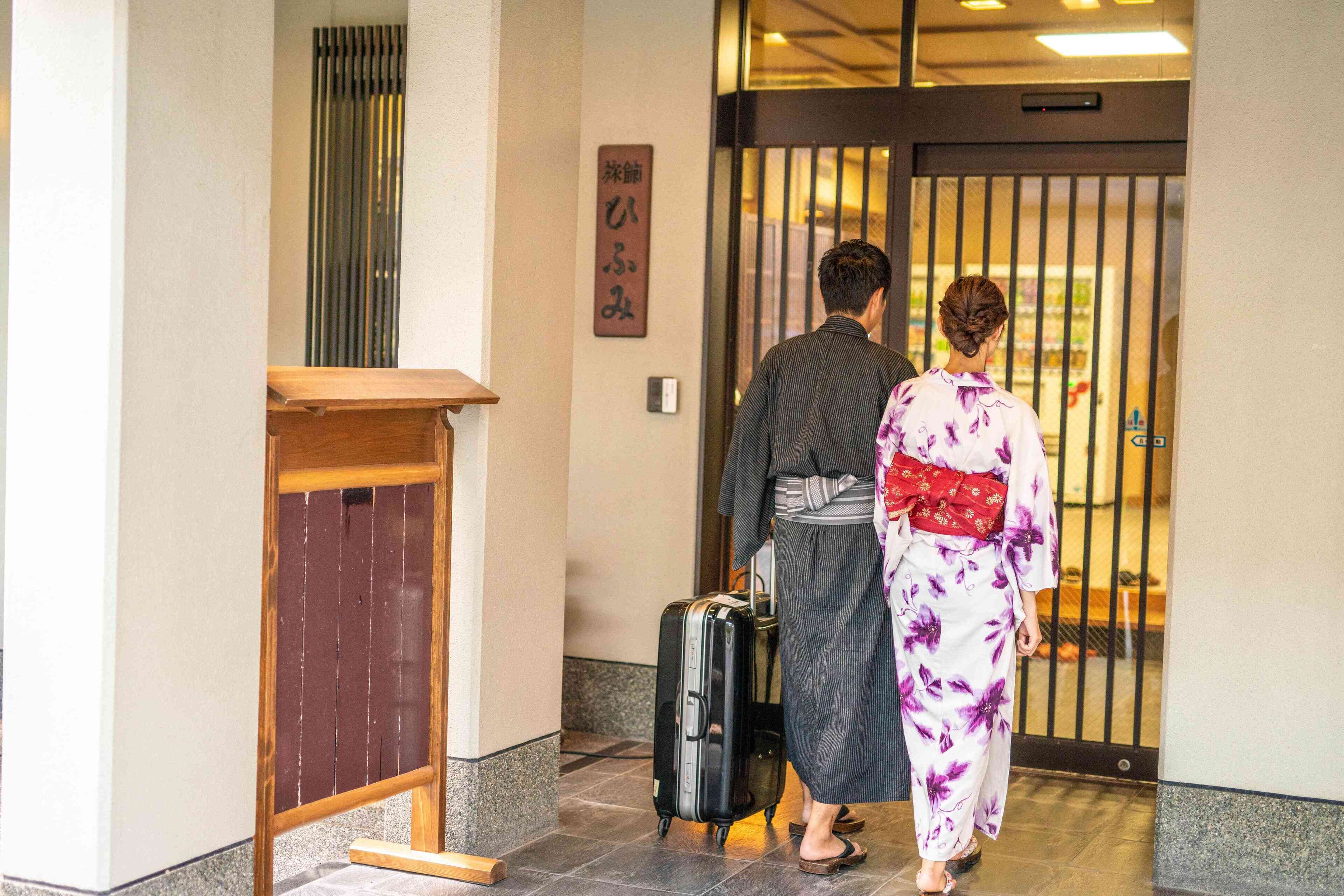 A man and a woman walking through a hotel entrance with a wooden counter and a sliding door.