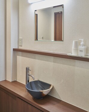 A bathroom with a vessel sink, a mirror, a hand soap dispenser, and a towel dispenser. - Hifumi Ryokan (Kyoto)